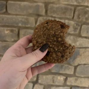 a lactation cookie held in the air in front of a rustic brick wall